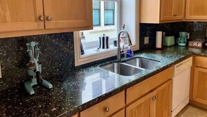 Una cocina con armarios de madera, encimera de granito, un lavamanos y una ventana con vistas.