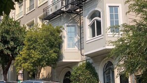 Un edificio de varios pisos con escalera de incendios, coches aparcados y zonas verdes.