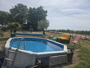 Una piscina al aire libre con terraza de madera, rodeada de césped y árboles.