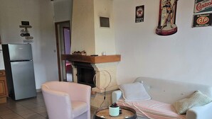 A living room with a sofa, a chair, a round wooden table, a fireplace, and a refrigerator. - Gîte les trois pierres (Riocaud)