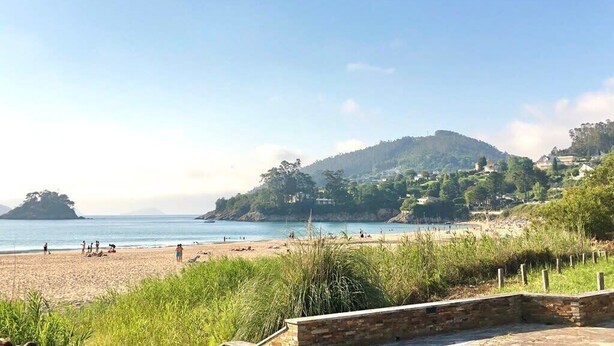 A beach with people, a hill with houses, and a clear sky. - The Cliffs - The Area Nightfall (Viveiro)