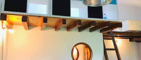 A room with a wooden beam ceiling, a round mirror, and a ladder.