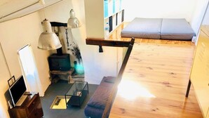 Ett rum i loftstil med trägolv, en bänk, ett skrivbord med en dator och en hängande lampa.