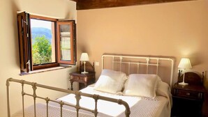 Un dormitorio con cama, mesitas de noche, ventana con cortinas y vistas a zonas verdes.