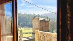 Una habitación con un ventanal grande que da a un muro de piedra y un edificio pequeño en un entorno rural.