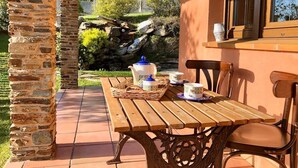 Una mesa de madera con sillas, un pilar de piedra y una ventana con vistas a la vegetación y rocas.