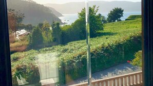 Vista a través de una ventana: cielo despejado, masa de agua y colinas a lo lejos.