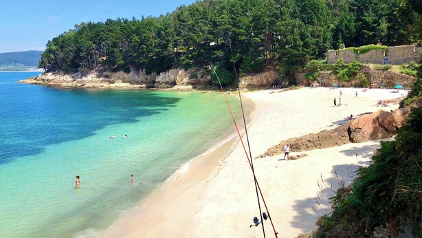 Una playa con agua turquesa cristalina, una orilla arenosa y un promontorio boscoso.