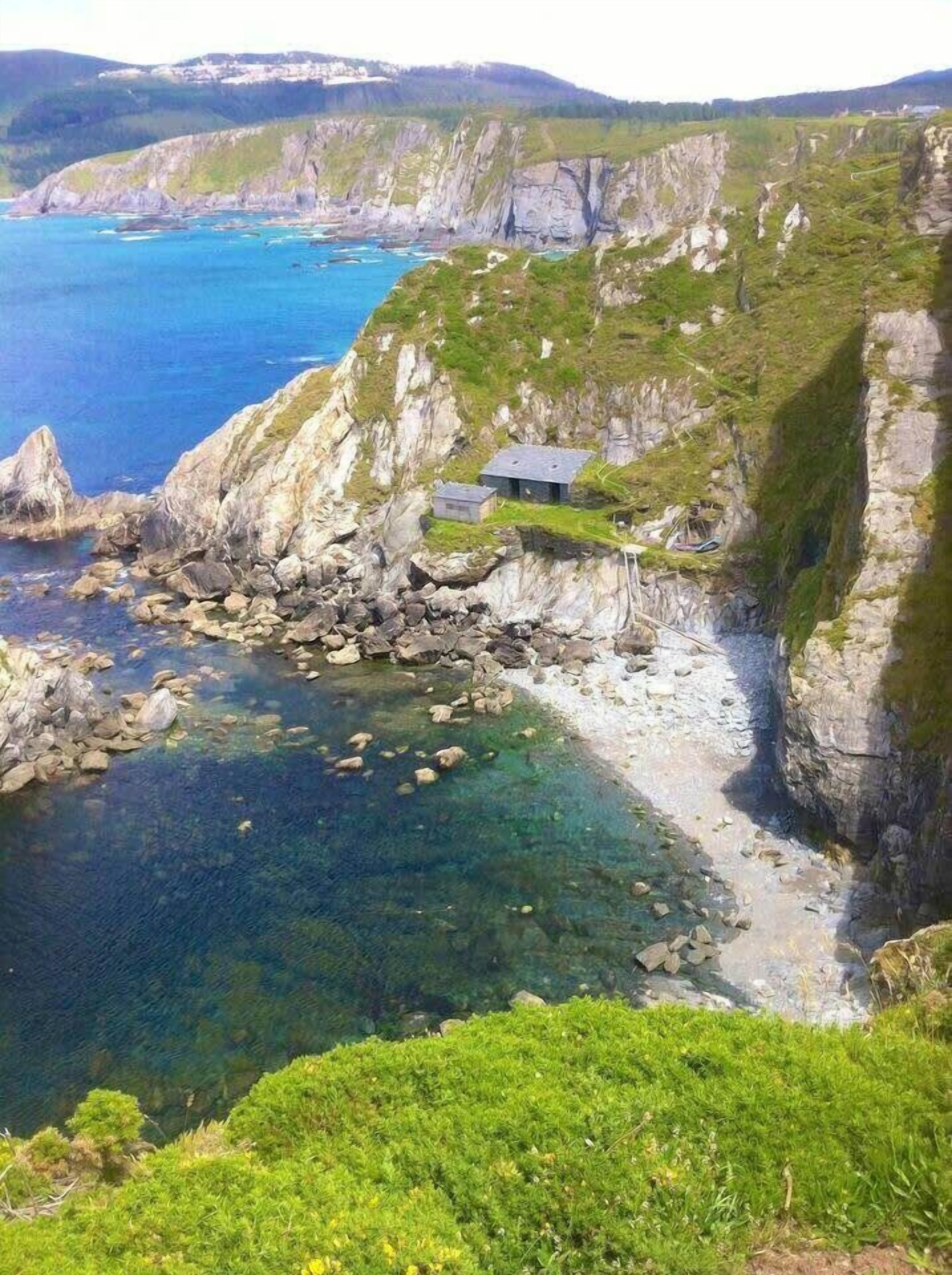 A coastal landscape with cliffs, clear water, and a small building on the shore.