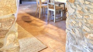 A rustic stone interior with a wooden ceiling, a dining table with chairs, and a door leading to another room. - The Cliffs - Cottage Xilloi Beach (O Vicedo)