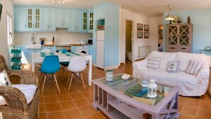 A cozy living room with a white sofa, a glass coffee table, and a dining area with a white table and blue chairs.