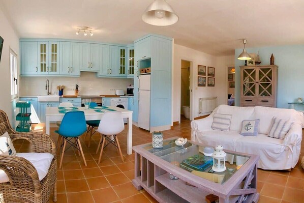 A cozy living room with a white sofa, a glass coffee table, and a dining area with a white table and blue chairs. - The Cliffs - Surf Lodge Esteiro (O Barqueiro)