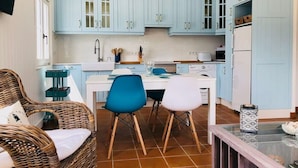 A compact kitchen with light blue cabinets, a dining table with two chairs, and a wicker chair with cushions.