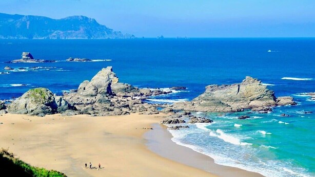 A coastal beach with rocky formations and clear blue water.