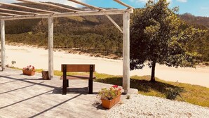 A wooden bench under a pergola with a view of a beach and hills.