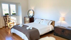 A bedroom with a large bed, a wooden dresser, a chair, and a small table.