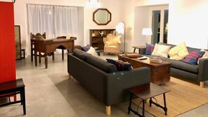 A living room with a sofa, a coffee table, a dining table with chairs, a fireplace, and a chandelier.