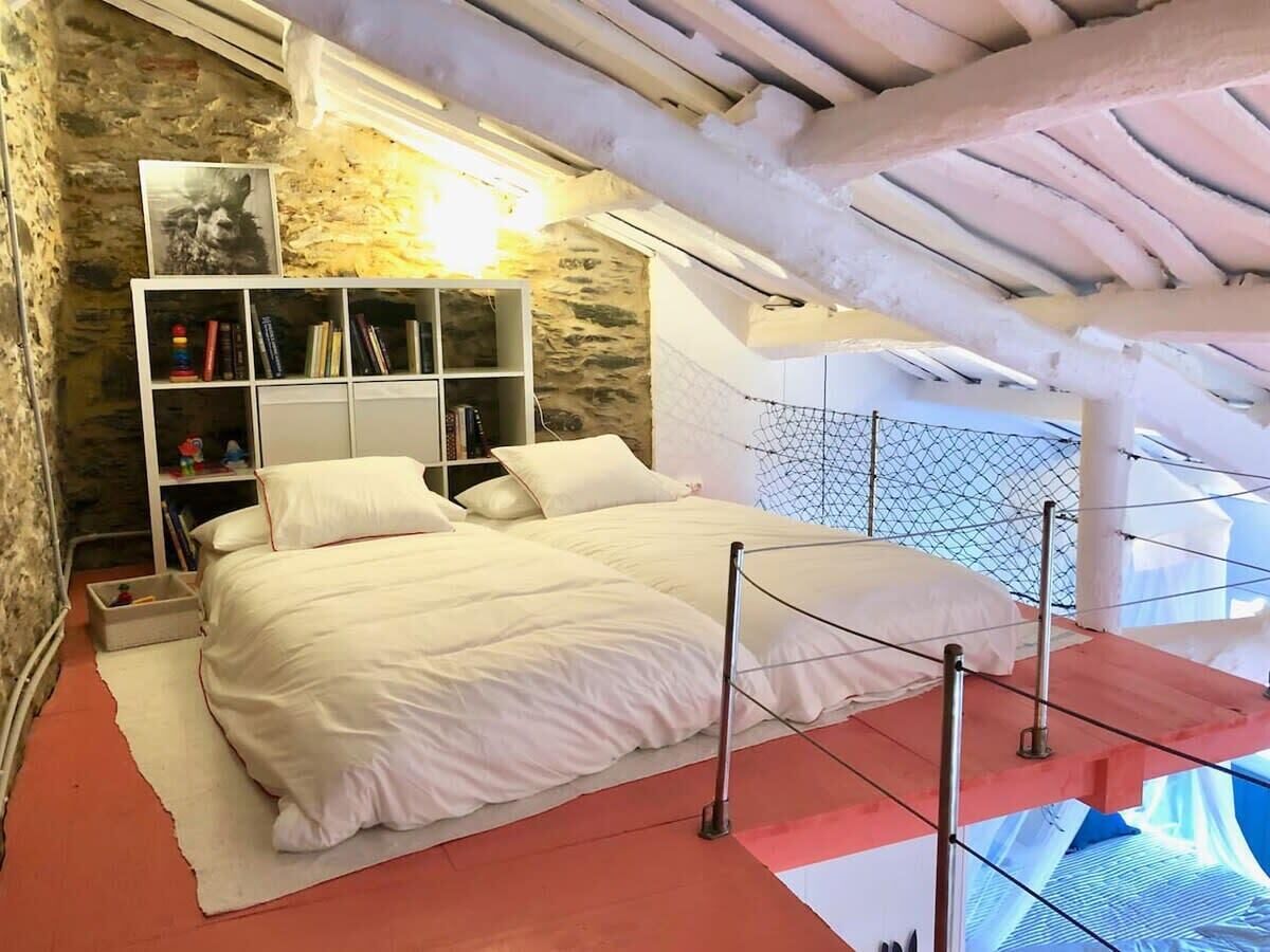 Un dormitorio con pared de piedra, una estantería blanca, una cama con ropa de cama blanca y una alfombra roja.