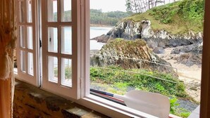 A room with a large window overlooking a rocky coastline with a view of the sea and trees. - The Cliffs - Cala Porto do Val (O Vicedo)