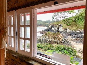 A room with a large window overlooking a rocky coastline with a view of the sea and trees.