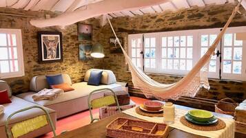 A rustic interior with a hammock, stone walls, a sofa, and a dining table with wicker baskets.