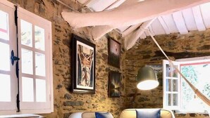 A rustic room with stone walls, a sofa with cushions, a basket of seashells, and a framed picture on the wall. - The Cliffs - Cala Porto do Val (O Vicedo)