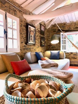 A cozy room with a stone wall, a sofa with cushions, a basket of seashells, and a framed picture on the wall.