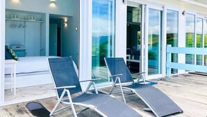Una terraza moderna al aire libre con dos sillones, una puerta de cristal que da a una habitación y una barandilla blanca.