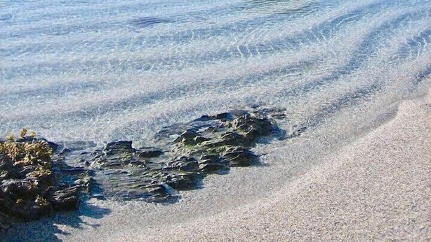 Un paisaje costero con agua cristalina, formaciones rocosas y una playa de arena.