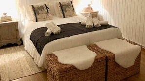 Un dormitorio con cama, mesitas de noche, un espejo y un banco de mimbre.