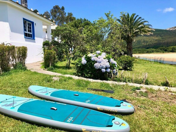 Two paddleboards on grass in front of a white building with a blue window. - The Cliffs - Esteiro Saltwater Beach (O Barqueiro)