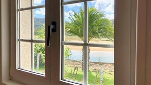 Una ventana con vistas a una playa, palmeras y una valla.