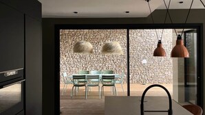 A modern kitchen with a stone wall, a dining area with chairs, and pendant lights.