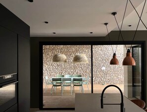 Una cocina moderna con pared de piedra, comedor con sillas e iluminación colgante.