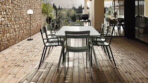A modern outdoor dining area with a stone wall, wooden flooring, and a hanging light fixture.