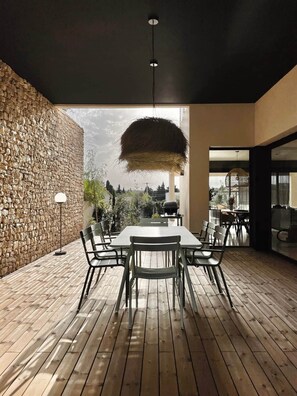 Un área de comedor exterior moderna con una pared de piedra, piso de madera y una lámpara colgante.