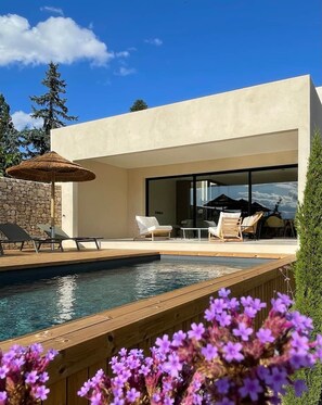 Un área de piscina moderna al aire libre con sillones de descanso y una mesa de comedor.