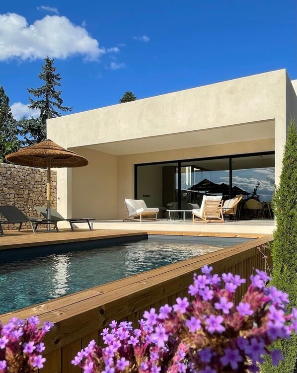 Un área de piscina moderna al aire libre con sillones de descanso y una mesa de comedor.