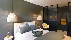 A modern bedroom with a large bed, two pendant lights, a bedside table, and a chair.