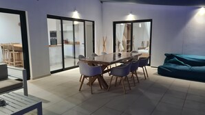 A modern dining area with a wooden table and chairs, a sofa, and a kitchen in the background.