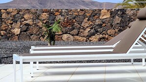 A beachside lounge area with white lounge chairs and a stone wall backdrop.