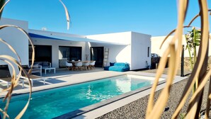 A modern house with a swimming pool, outdoor seating, and a ladder leading to a balcony.