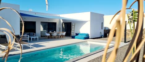 A modern house with a swimming pool, outdoor seating, and a ladder leading to a balcony.