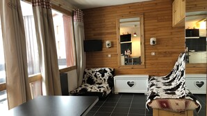 Ein gemütliches Zimmer mit einer Holzwand, einem großen Spiegel, einem schwarzen Fliesenboden und einem Stuhl mit Kuhmuster.