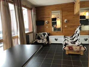 Ein gemütliches Zimmer mit einer Holzwand, einem großen Spiegel, einem schwarzen Fliesenboden und einem Stuhl mit Kuhmuster.