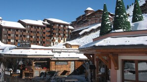 Ein schneebedecktes Resort mit mehrstöckigen Gebäuden, Außenbereichen zum Sitzen und schneebedeckten Bäumen.