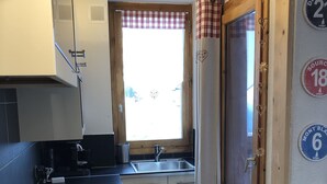 Eine kleine Küche mit schwarzem Arbeitsplatz, einem Spülbecken und einem Fenster mit Karottenmuster-Vorhang.