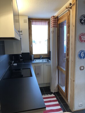 Eine kleine Küche mit schwarzem Arbeitsplatz, einem Spülbecken und einem Fenster mit Karottenmuster-Vorhang.