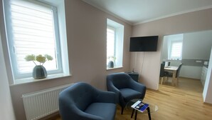 A modern living room with two dark armchairs, a glass coffee table, and a flat-screen TV mounted on the wall. - Beautiful three room apartment. Bright, stylish, cozy (Sachsen - Borna)