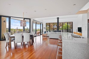 A modern kitchen with a large island, a dining area with chairs, and a living room with a sofa and a television. - St Johns Wood Treehouse (Blairgowrie)